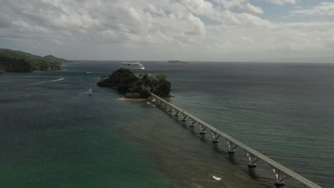 Aufsteigende-Luftaufnahme-Der-Fußgängerbrücke-In-Der-Bucht-Von-Samana-Mit-Dem-Luxuskreuzfahrtschiff,-Das-Den-Hafen-An-Einem-Sonnigen-Tag-In-Der-Dominikanischen-Republik-Verlässt