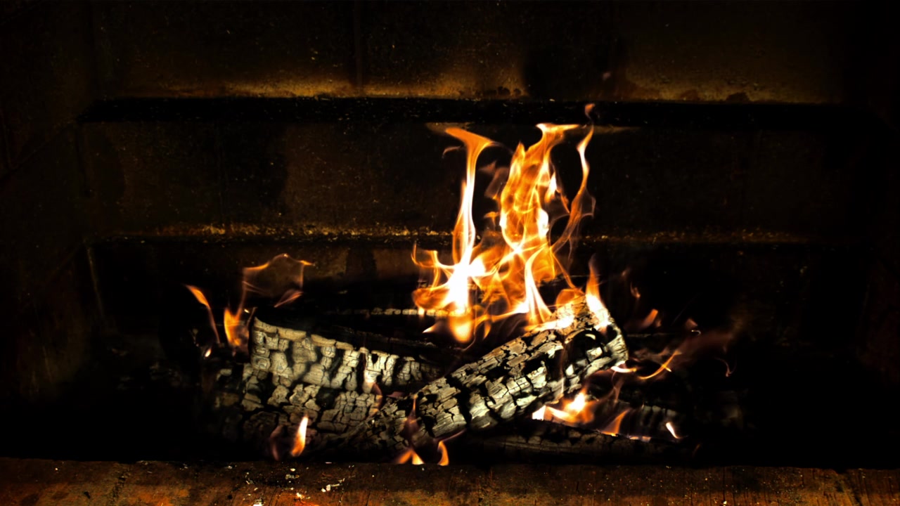 Primo piano di fuoco che arde e crepita in un camino buio.