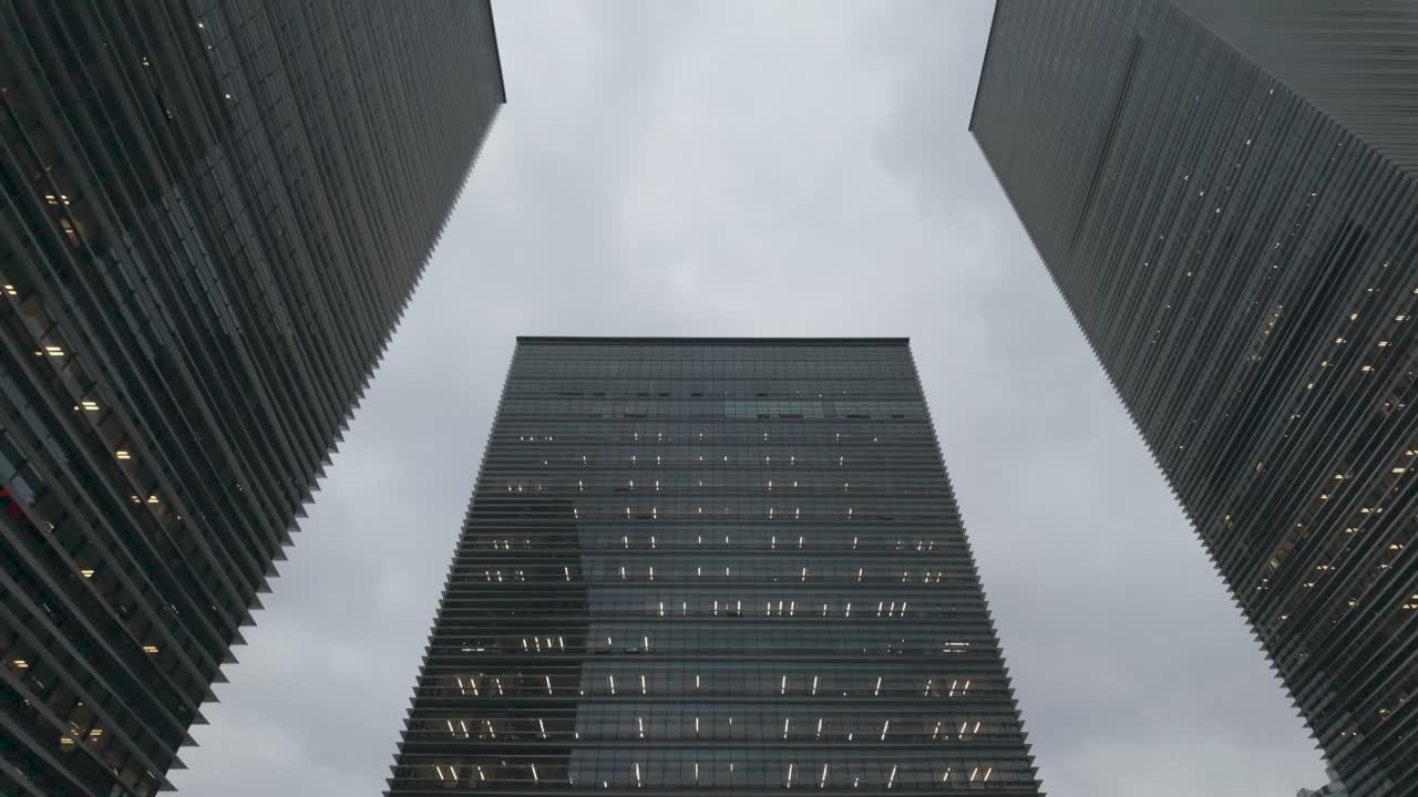 Slow-motion video looking up at three modern high-rise glass skyscrapers against a gray sky in Shanghai