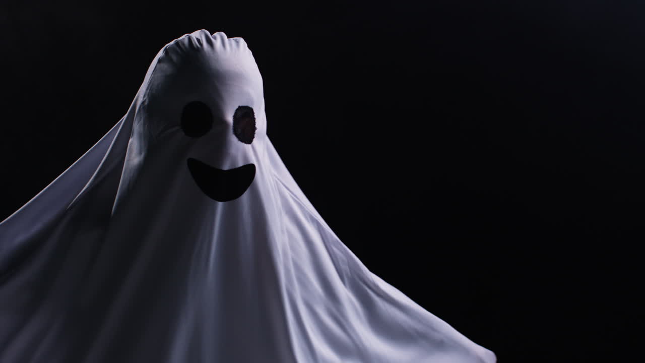 Child Dressed Up In Ghost Costume Trick Or Treating At Halloween Scaring People In Front Of Black Studio Background 1