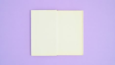 white hardcover opened book appear on purple theme, close and open again. stop motion flat lay