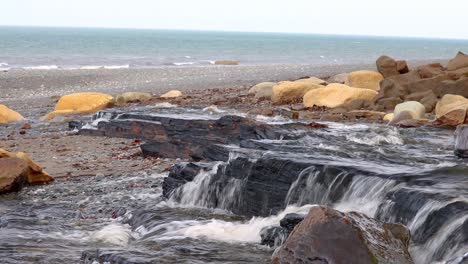 water flowing from a wide stream flowing over rocks creating a small waterfall on beach in kenai peninsula of alaska