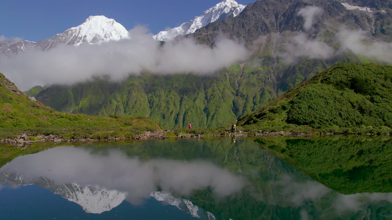 paisaje de nepal disparado por un avión no tripulado colinas verdes y nubes de montaña, chica caminando con un sari rosa, reflejo del lago 4k