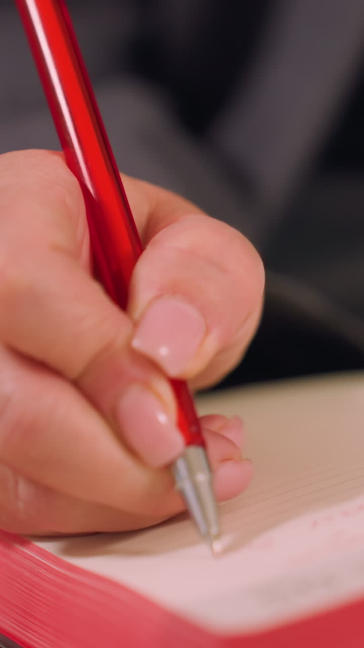 Close-up of hand holding red pen writing in open notebook. Focus on journaling, note-taking, and professional planning. Creative workspace, productive business environment, action in modern office