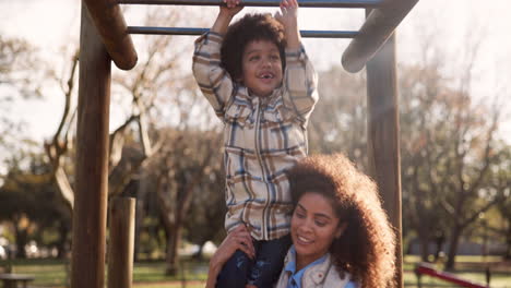 child playing on monkey bars with mother in park