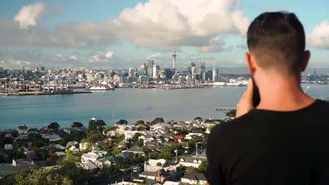 caucasian male from behind taking photo of auckland downtown, new zealand