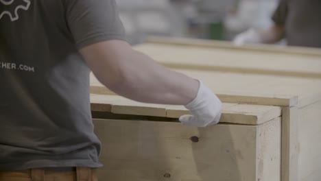 medium shot of two workers with gloves carefully putting a wooden lid on a large wooden box in a documentary-style handheld shot, all in focus