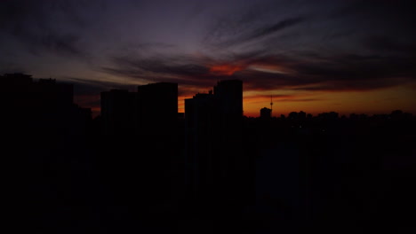 the drone descends over the city, silhouettes of skyscrapers against the background of a bright orange warm sky