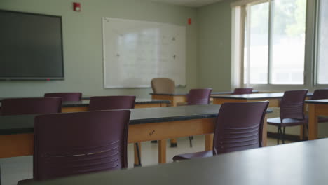 daylit school classroom with maroon chairs, wood desks, whiteboard, and flat screen monitor