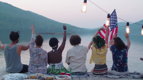 friends waving arms and swinging us flag on lake pier