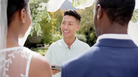 biracial man officiating wedding ceremony for african american couple in sunny garden, slow motion