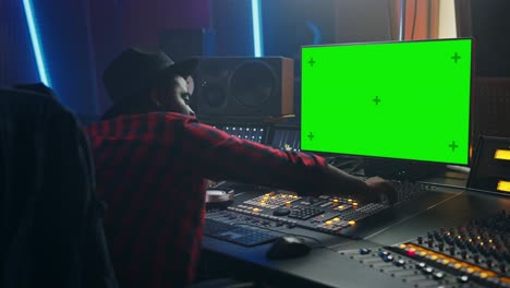 retrato de un elegante productor de audio que trabaja en un estudio de grabación de música, utiliza una computadora de pantalla verde, una placa de mezcla, un escritorio de control para crear una nueva canción.