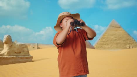 asian boy with a hat standing doubtfully and asking why after looking through the binoculars. boy researcher examines something while traveling in giza pyramid, travel tourism adventure concept