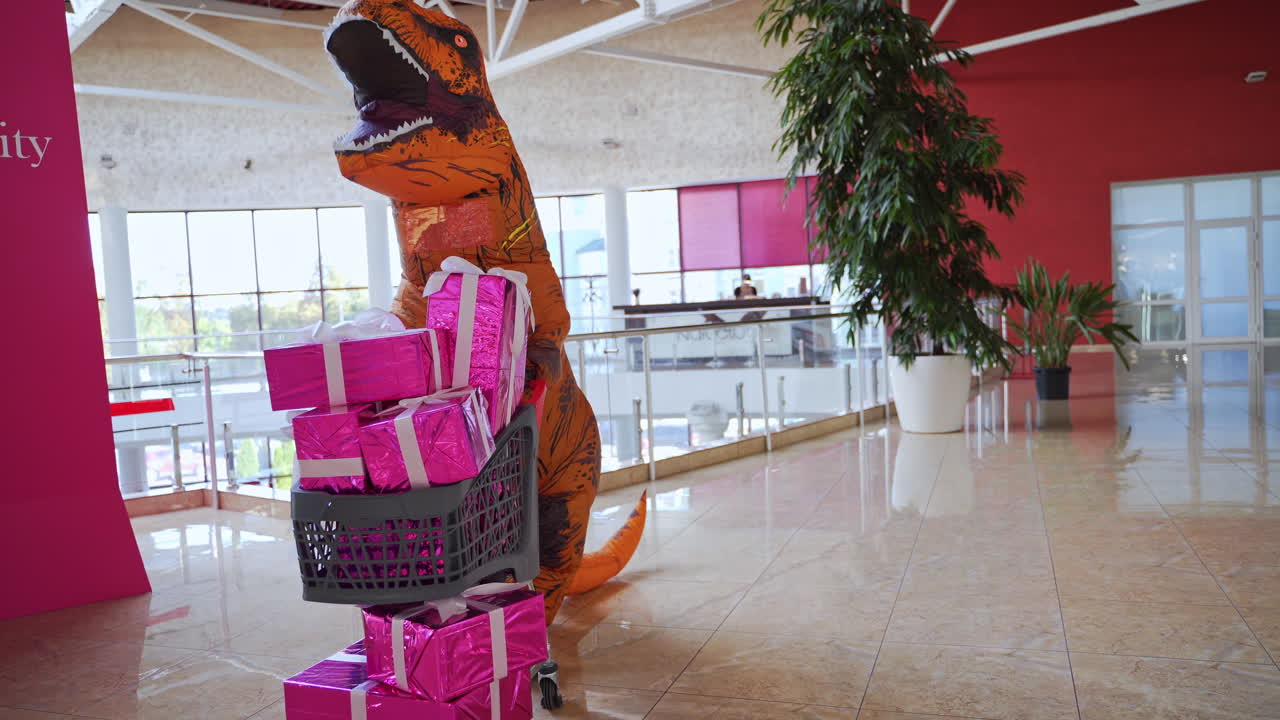 Man in the dinosaur costume is rolling the cart full of presents. Orange spotty dinosaur doing the shopping in the big mall.