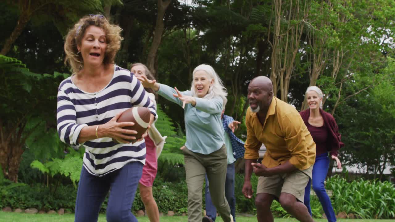 animación de felices y diversas mujeres y hombres amigos mayores jugando al fútbol americano en el jardín