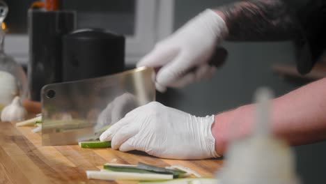 fresh zucchini being sliced on wooden board by young professional male chef in an elegant black shirt with tattoos