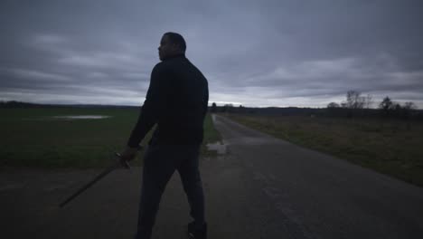 Modern-Black-Swordsman-Warrior-Awaiting-Battle-Opponent-in-Open-Field-Under-Grey-Sky,-Europe,-4K-|-Muscular,-Intimidating,-Shadow,-Figure,-Blurry,-Dark-Clothes,-Powerful,-Walking,-Investigate