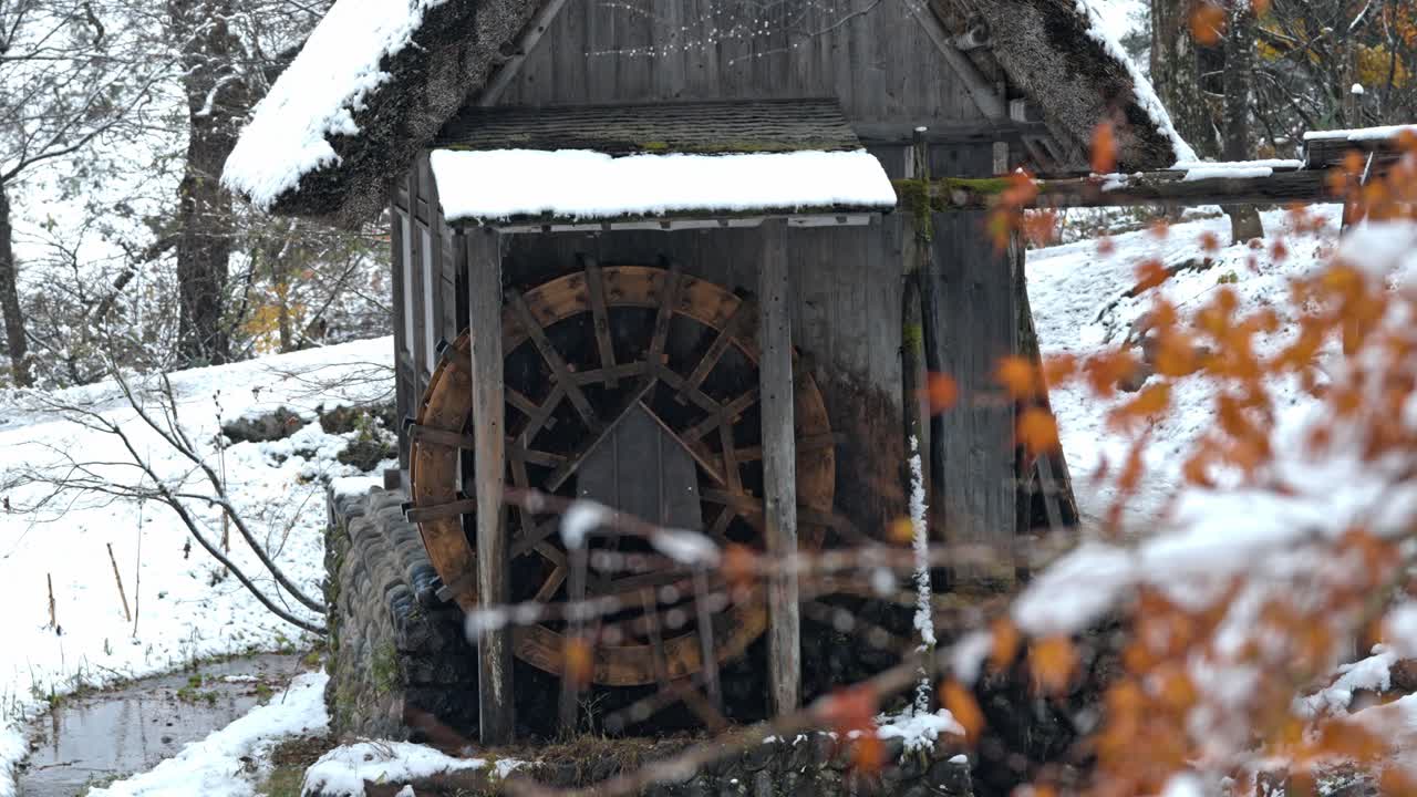 A traditional water mill stands quietly in Shirakawa-go, Japan, as snow gently falls around it.