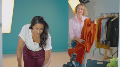 Fotógrafa-De-Moda-Femenina-Madura-Con-Asistente-Mirando-La-Ropa-Antes-De-Disparar-En-El-Estudio