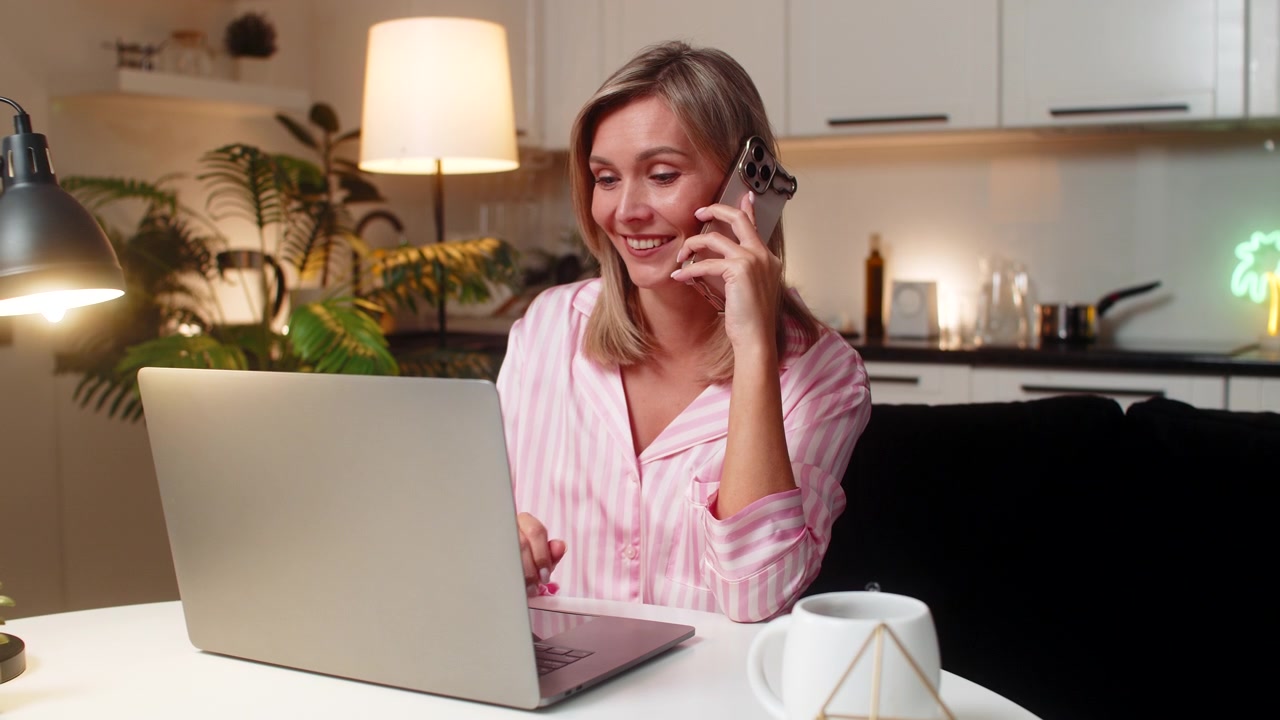 Donna adulta che lavora al portatile mentre parla al telefono, multitasking produttivo in remoto, voce chiara, chiamata mirata