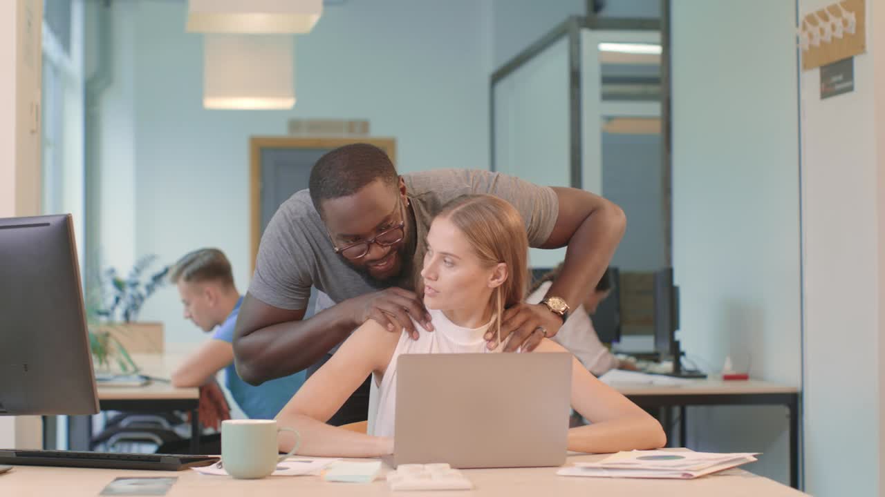 Pretty woman working on computer at coworking. Black man making massage