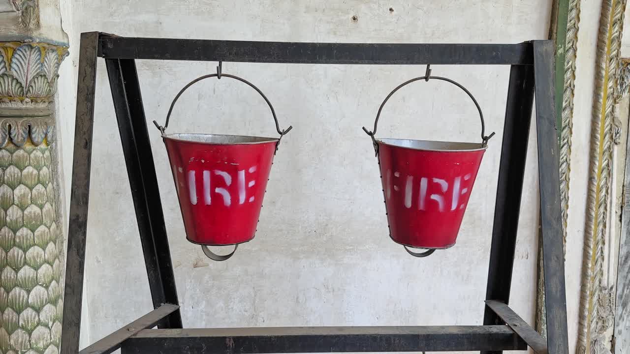 Un'inquadratura statica di due secchi antincendio rossi su un supporto di metallo, che evidenzia la tradizionale preparazione alla sicurezza antincendio, la chiara visibilità e il rapido accesso manuale in caso di emergenza