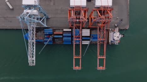 overhead view of crane loading cargo ship with intermodal containers at haina occidental port in dominican republic. - aerial shot