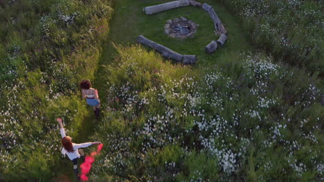 drone shot of two female friends camping at music festival running through field with smoke flare