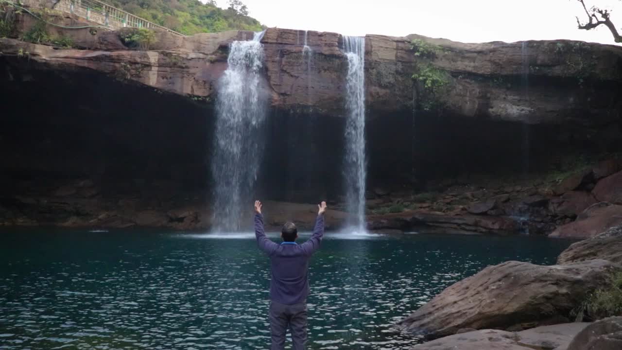 krangsuri 폭포 meghalaya 인도에서 찍은 아침 비디오에서 산 정상에서 떨어지는 자연 폭포를 즐기는 젊은 남자