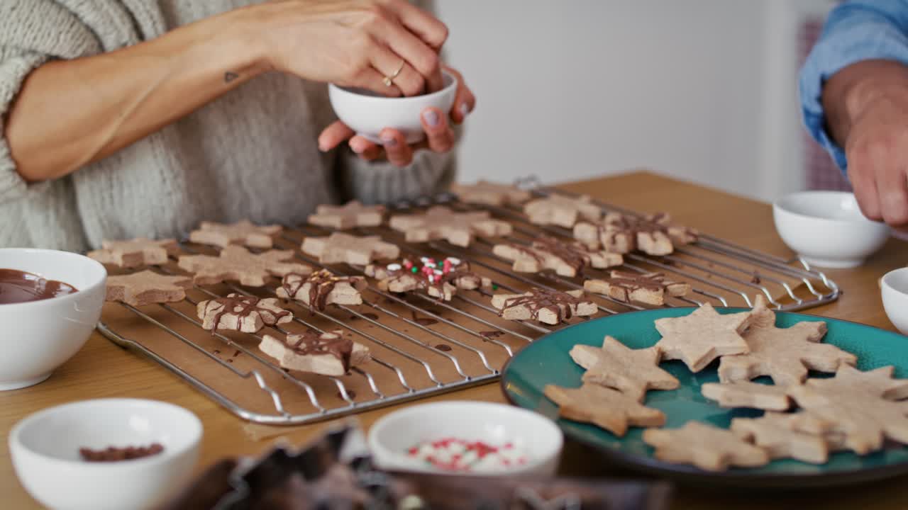 pareja multiétnica irreconocible decorando galletas dulces con salpicaduras coloridas durante la navidad.