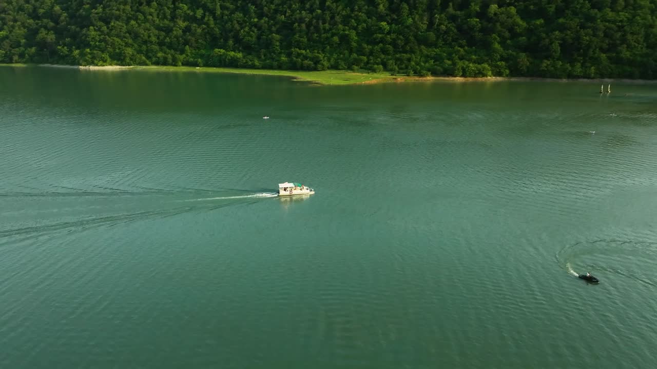Luftaufnahme eines kleinen Boots, das über einen ruhigen Bergsee in Georgia fährt, umgeben von grünen Hügeln und unberührter Natur