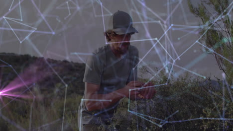 Man crouching in arid scrubland, inspecting plant samples, showing technology network overlay