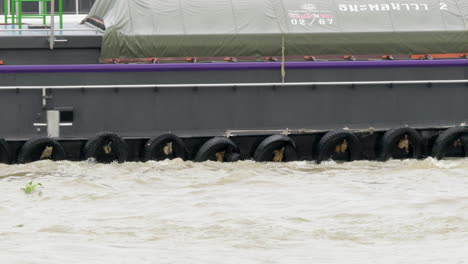 cargo barges moving along the flooded chao phraya river, a major waterway in the city of bangkok in thailand.