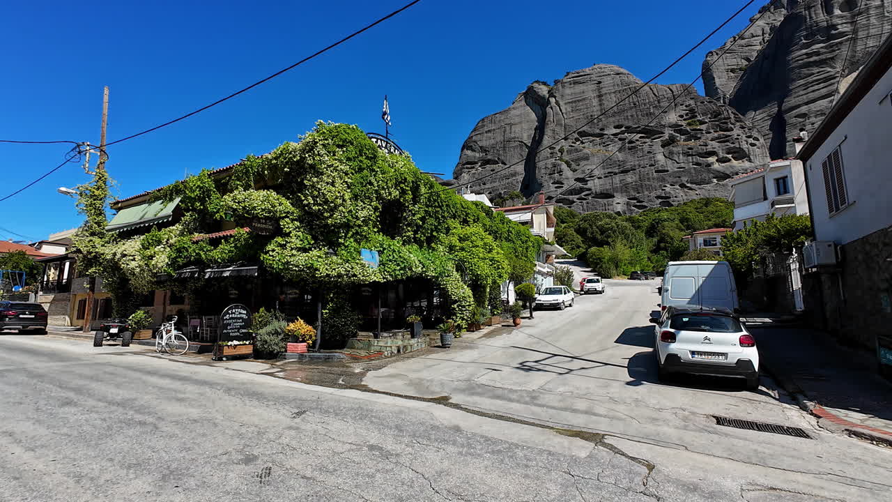 Village street with a vine-covered building and large rock formations under a clear sky