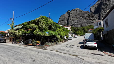 village street with a vine-covered building and large rock formations under a clear sky
