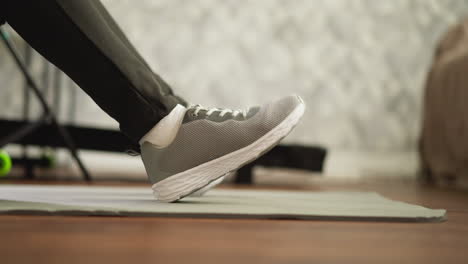 woman does relaxing exercises for feet on floor closeup. athletic lady in sneakers and leggings warms up ankles in domestic gym. home fitness routine