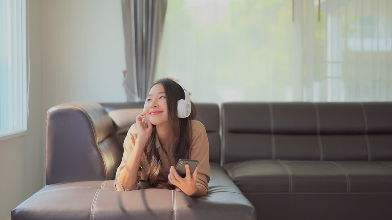 Pretty Woman Laying on the Sofa Listens to Music via Smartphone SLOMO