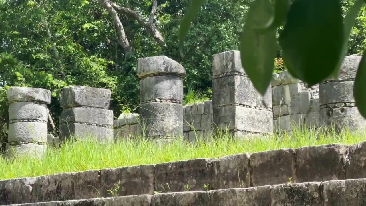 メキシコ、ユカタン州のチチェン・イッツァにある千本柱のグループを、前景の植物と共に手持ちでワイドにパン撮影したショット。4K。