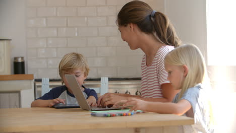 mamá y los niños usando computadoras y dibujando en la mesa de la cocina