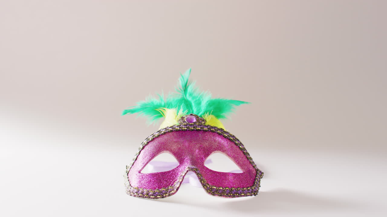 video de máscara de mascarada rosa con plumas verdes y amarillas sobre fondo blanco con espacio de copia