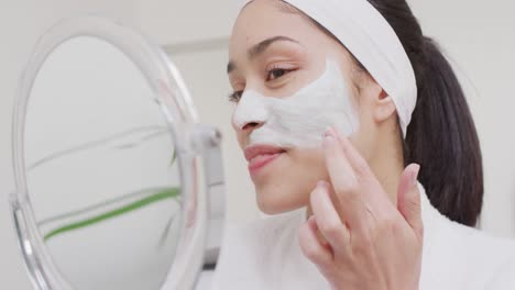 Biracial-woman-with-band-applying-cream-on-face-in-bathroom