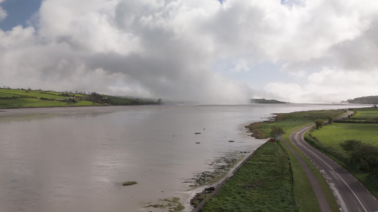 Drone aerial coastal road in West Cork with lifting ocean mist and wall of clouds on a blue sky, Courtmacsherry Ireland