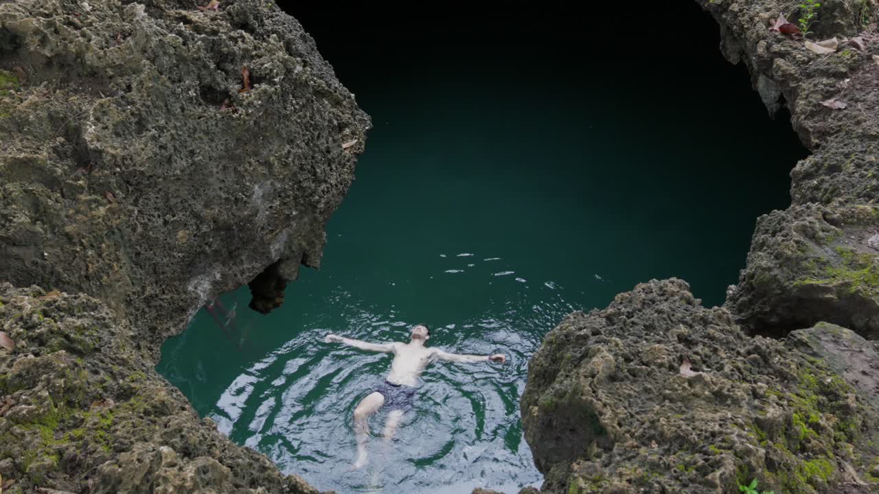 nadador flotando en las aguas claras de la cueva de la piscina de cabagnow, filipinas, rodeado de escarpados acantilados