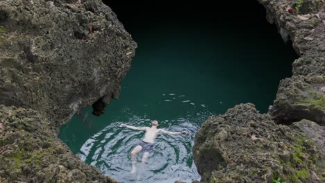 swimmer floating in the clear waters of cabagnow pool cave, philippines, surrounded by rugged cliffs