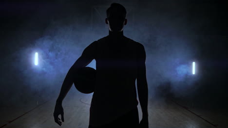 basketball player knocks the ball in the light of the lamps shining behind stands in the duma and knocks the ball on the floor in the basketball hall in slow motion