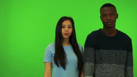 a young black man and a young asian woman show thumbs down to the camera - green screen studio