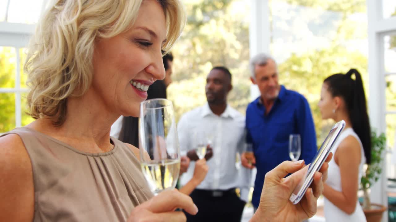 donna sorridente che usa un telefono cellulare mentre gli amici interagiscono sullo sfondo