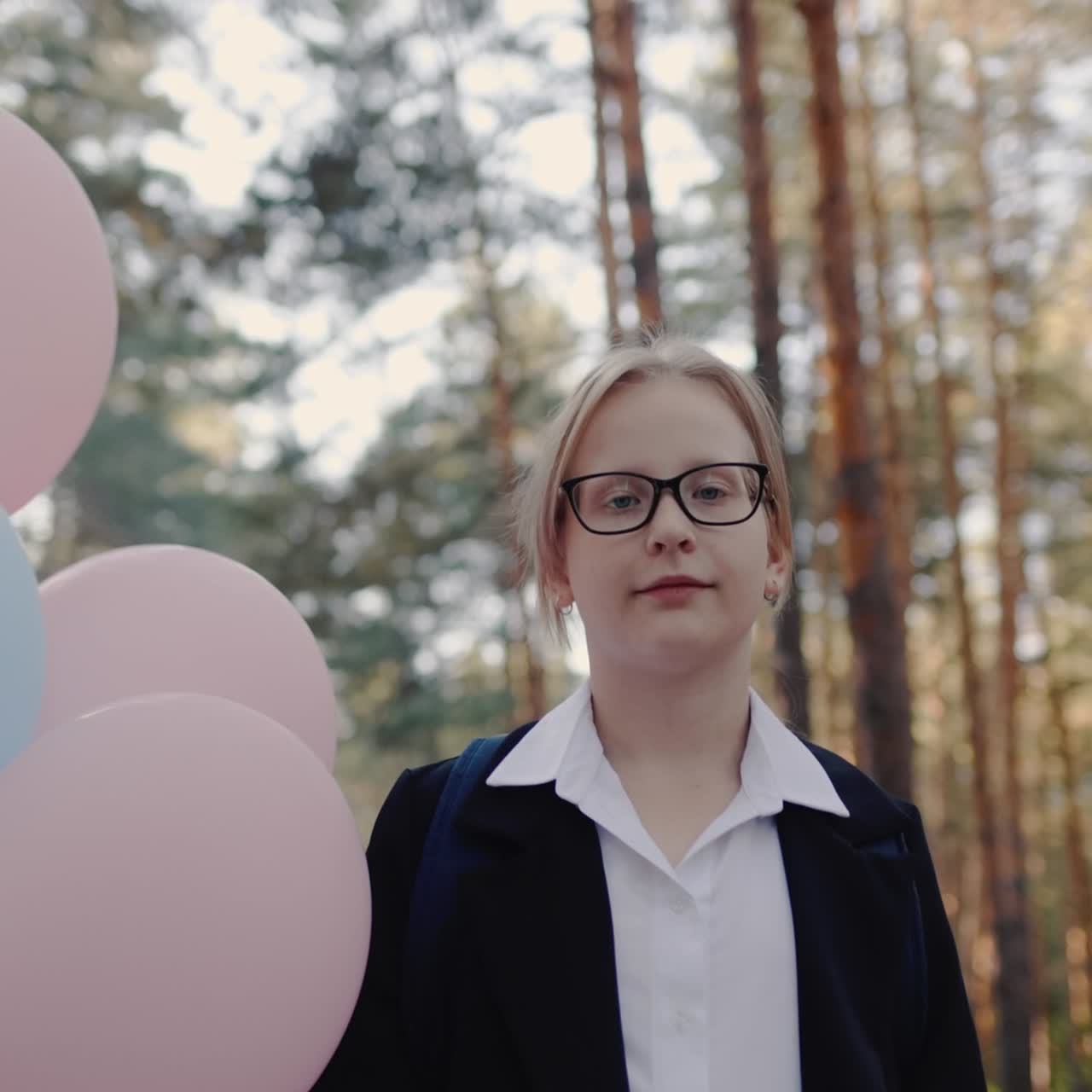 retrato de una colegiala con globos en un parque con pinos altos