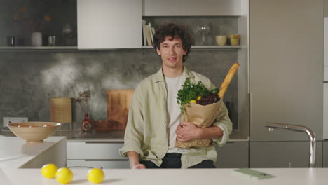 a young man holding a bag of groceries in a modern kitchen