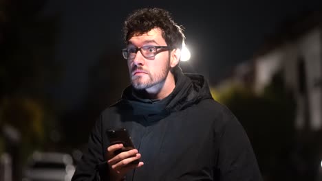 Young-Man-stands-in-cold-winter-night-in-german-suburb-around-munich-and-is-scrolling-on-his-phone,-using-technology